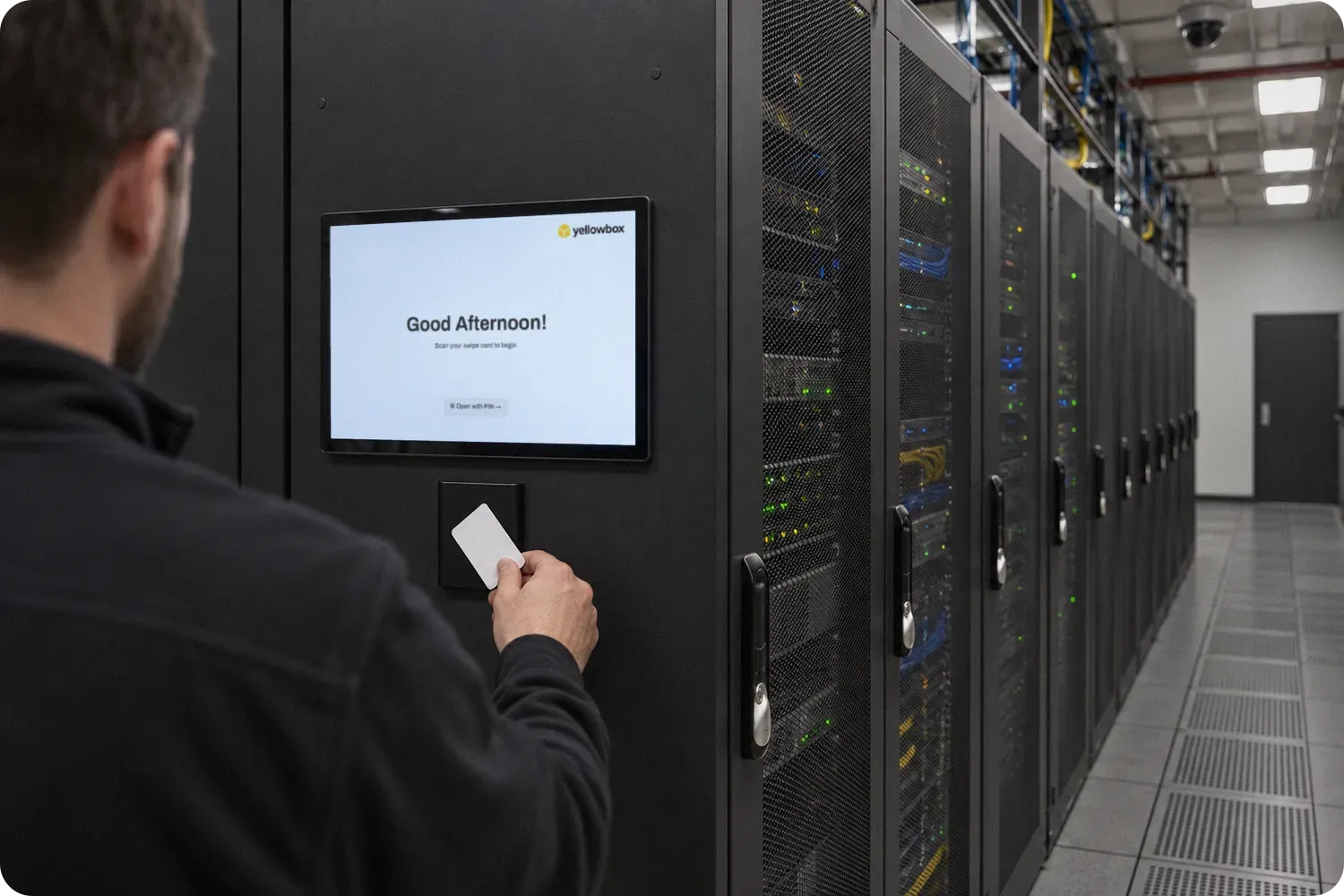 Technician tapping an access card on the reader of a Yellowbox Kiosk mounted at the end of a server cabinet row.